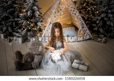 Happy funny child girl with gifts at the Christmas tree.  Little girl picture in the New Year decorations.  New Year's advertising.  Photo studio with christmas decoration.