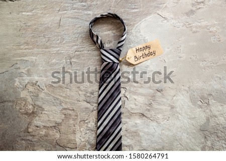 Man's birthday concept. Happy birthday text near men's tie on grey background top view.