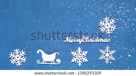 Decorative wooden Christmas snowflakes and sleighs on blue background. Festive New Year card in trendy color. Copy space