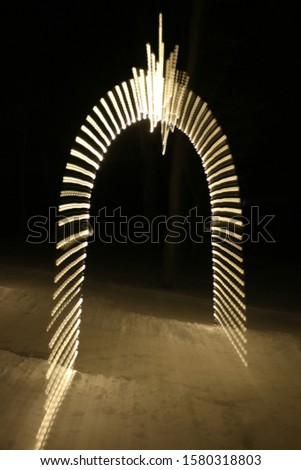 White lights on an archway are taken with an intentionally slow shutter speed and zooming the lens in while taking the photo, to create abstract light trails at night.