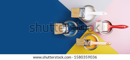 Banner with four open cans of paint with brushes on them on bright symmetry background. Yellow, white, pink, blue colors of paint. Top view. Royalty-Free Stock Photo #1580359036