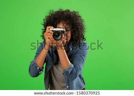 Portrait of happy black female photographer taking a photo. Young pretty woman shooting with camera on greenscreen