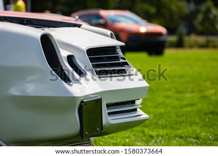 Classic American white muscle fast car front with Sharp features, on the grass of outdoor show, with open hood, blurred cars in the background