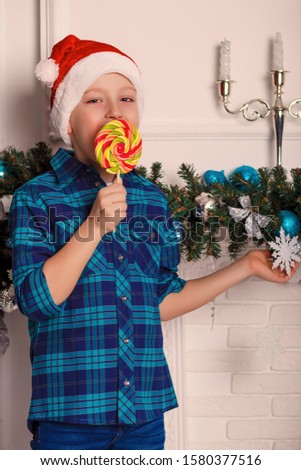 Little boy in santa claus hat holds a big tasty lollipop in his hand. The child is happy with New Year's gift. Happy new year. Portrait. Funny photo