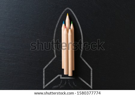Drawing of a rocket on a black metal background with pencils. Startup concept
