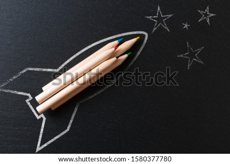 Drawing of a rocket on a black metal background with pencils. Startup concept