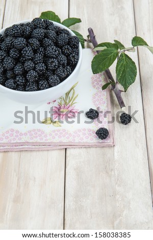 A bowl with ripe wild blackberries on an old wooden background