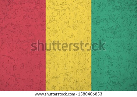 Guinea flag depicted in bright paint colors on old relief plastering wall. Textured banner on rough background