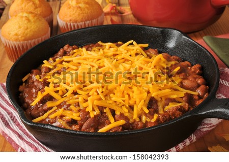 Chili con carne in a cast iron skillet topped with cheddar cheese