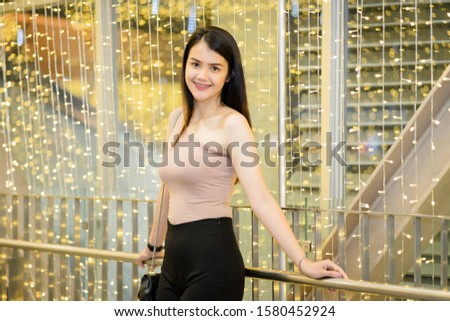 A cheerful Asian woman enjoys taking photo with light bokeh background decoration for the Christmas festival and new year celebration.