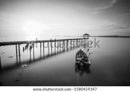 Long exposure shot of seascape with boat and jetty background in black and white. Soft focus due to long exposure shot.