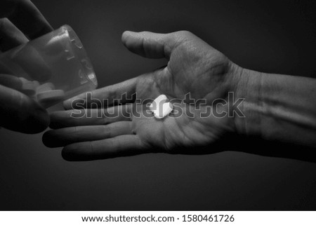 Man's left hand holding bottle pours two opioid capsules into right hand in front of neutral black and white background