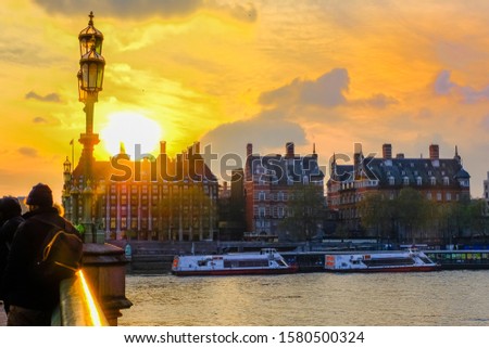 View of downtown district in London, England, from London Bridge at sunset; River Thames in foreground; dramatic sky