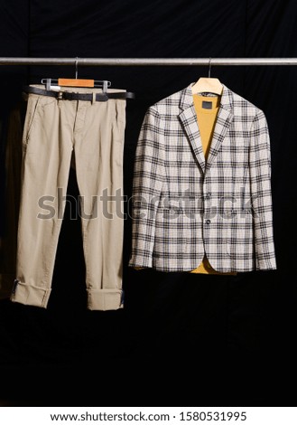 Men's striped suit and yellow sweater and pants 
 on hanger on black background

