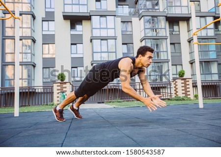 Strong muscular mixed race black man working out in outdoor gym sportsground. Crossfit training. Making push-ups. Workout open air on urban background.