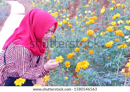 Hijab woman enjoys the flower garden in the top of the hill in Eling Bening in Ambarawa,Central Java,Indonesia with mountain and cloudy sky background.
