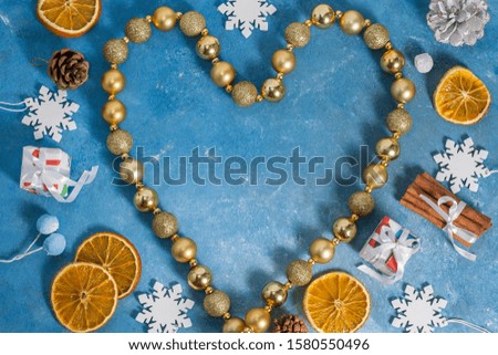 Christmas and New Year pattern from hearts made of garlands, snowflakes, cookies, cinnamon, orange, cones and marshmallows on a blue background with stars. Flat lay, top view, copy space.