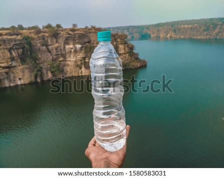 A picture of drinking water bottle in hand in front of a river which remembers the importance or saving of the water