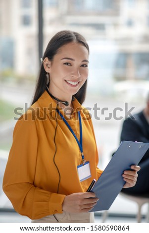 Good mood. Young pretty asian woman with a badge smiling nicely