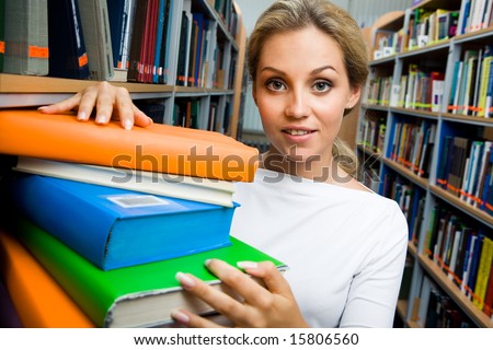 Portrait of pretty student standing by the stack of books in the aisle of library