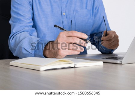 Businessman using laptop. Man holding in his hands eye glasses and a pen next to the notebook at office desk.