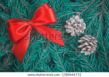 Flat lay a large beautiful bow of red silk ribbon and two cones covered with hoarfrost on fluffy blue spruce branches with copy space. Design template for Christmas, New Year greeting card or banner.