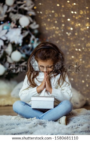Happy little child girl with gift box sitting near decorated xmas tree with light. Merry Christmas. girl dreams about a gift