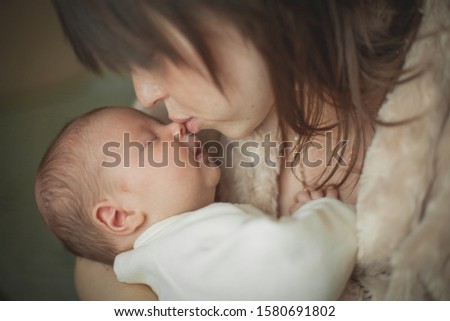 Mom gently kisses a newborn boy, holding in her arms.