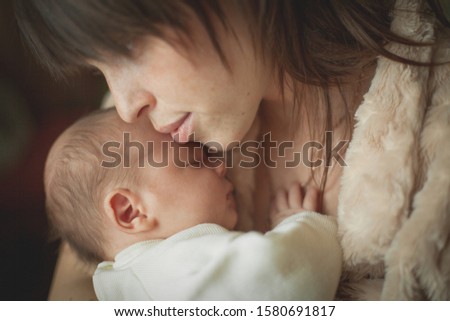 Mom gently kisses a newborn boy, holding in her arms.