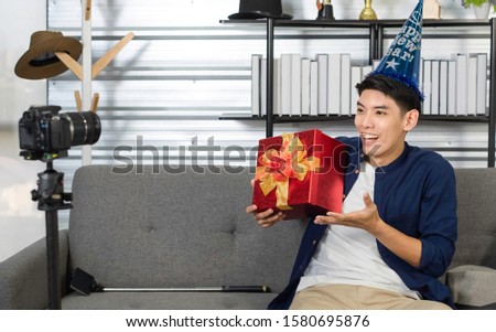 Asian Youtuber / vlogger live streaming on Facebook, holding Christmas gift box in front of camera. Youtuber selling Christmas gift online using social media for online business. New Year sale concept