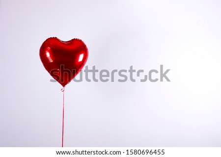 Celebrating Saint Valentine's Day with heart shaped red foil air balloon. Gift for loved woman on special occasion with romantic symbols, Women`s day. Close up, copy space, background, isolated.