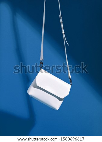 Levitating female white sneakers and small stylish cross body bag on deep classic blue background. Minimalist stylish female accessory.  Color of the year 2020. Main color trend. Summer sale concept.  Royalty-Free Stock Photo #1580696617