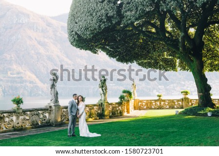 Villa Balbianello wedding photoshoot beautiful couple bride and groom long veil and white dress on mountains background lake Como Italy ceremony luxury beautiful sunny day