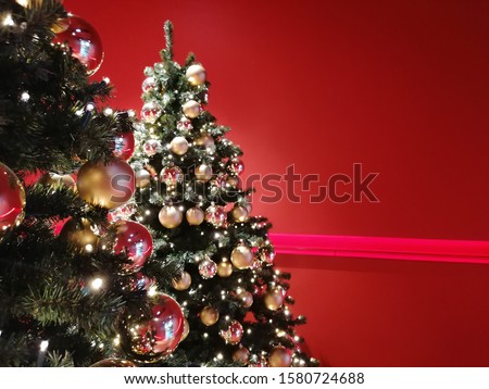Christmas tree on red background.  Glass balls, garland and Christmas decorations on green branches.  Red wall as background. Copy space. Plase fo text. 