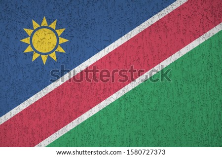Namibia flag depicted in bright paint colors on old relief plastering wall. Textured banner on rough background
