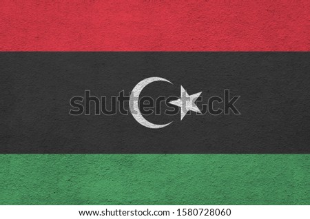 Libya flag depicted in bright paint colors on old relief plastering wall. Textured banner on rough background