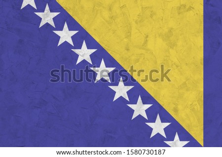 Bosnia and Herzegovina flag depicted in bright paint colors on old relief plastering wall. Textured banner on rough background