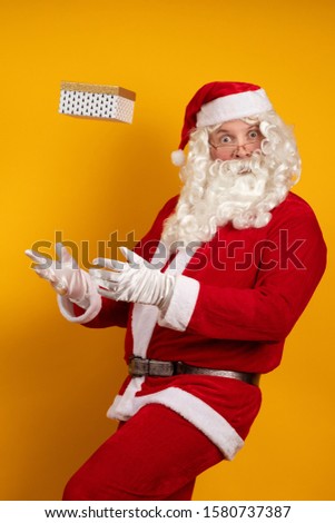 Santa Claus holds a box with a gift in his hands, juggles and poses on a yellow background