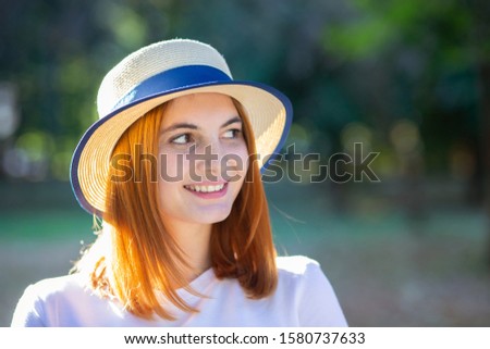 Closeup portrait of redhead hipster teenage girl in yellow hat smiling outdoors in sunny summer park.