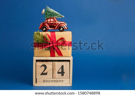 Brown gift boxes with red ribbons and fir tree branch, red toy car and Calendar on blue trendy background. Color of the year. Present for Christmas. December 24