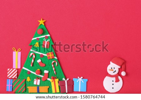 a handmade clay sculpture snowman stands beside a Christmas tree with ornaments and gift boxes