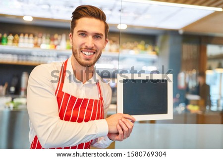 Waiter holding a blank chalkboard in bar or restaurant in his hands