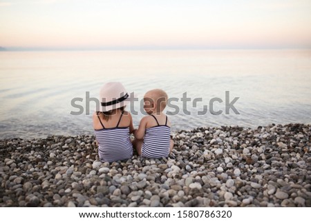 adorable Caucasian children in swimsuits on a pebble beach by the sea, a child in a hat with his sister looks at the sea. The concept of rest and children, child safety