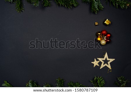 Christmas ornaments (Christmas baubles, stars and little presents) on black background framed by fir twigs