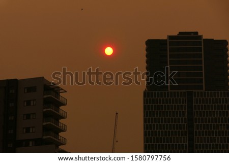 
Australian bushfires 2019: The glowing red sun is barely visible through the thick smoke from nearby wild fires. Tall building silhouettes and dark sky. Catastrophic fire danger Sydney NSW Australia Royalty-Free Stock Photo #1580797756