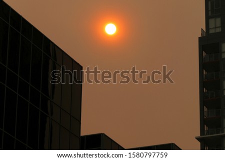 
Australian bushfires 2019: The glowing red sun is barely visible through the thick smoke from nearby wild fires. Tall building silhouettes and dark sky. Catastrophic fire danger Sydney NSW Australia Royalty-Free Stock Photo #1580797759