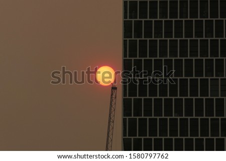 
Australian bushfires 2019: The glowing red sun is barely visible through the thick smoke from nearby wild fires. Tall building silhouettes and dark sky. Catastrophic fire danger Sydney NSW Australia Royalty-Free Stock Photo #1580797762