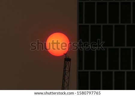 
Australian bushfires 2019: The glowing red sun is barely visible through the thick smoke from nearby wild fires. Tall building silhouettes and dark sky. Catastrophic fire danger Sydney NSW Australia Royalty-Free Stock Photo #1580797765
