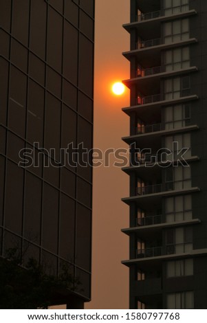 
Australian bushfires 2019: The glowing red sun is barely visible through the thick smoke from nearby wild fires. Tall building silhouettes and dark sky. Catastrophic fire danger Sydney NSW Australia Royalty-Free Stock Photo #1580797768