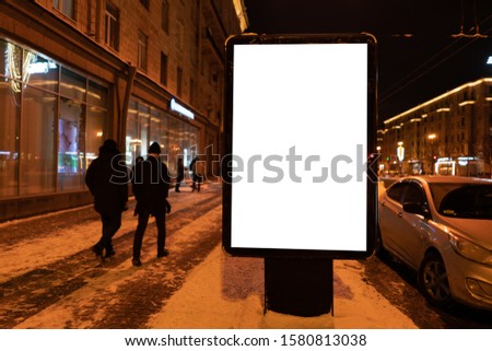 Vertical billboard in the winter at night in the city. with people walking in the city Ad design MOCKUP with white field.